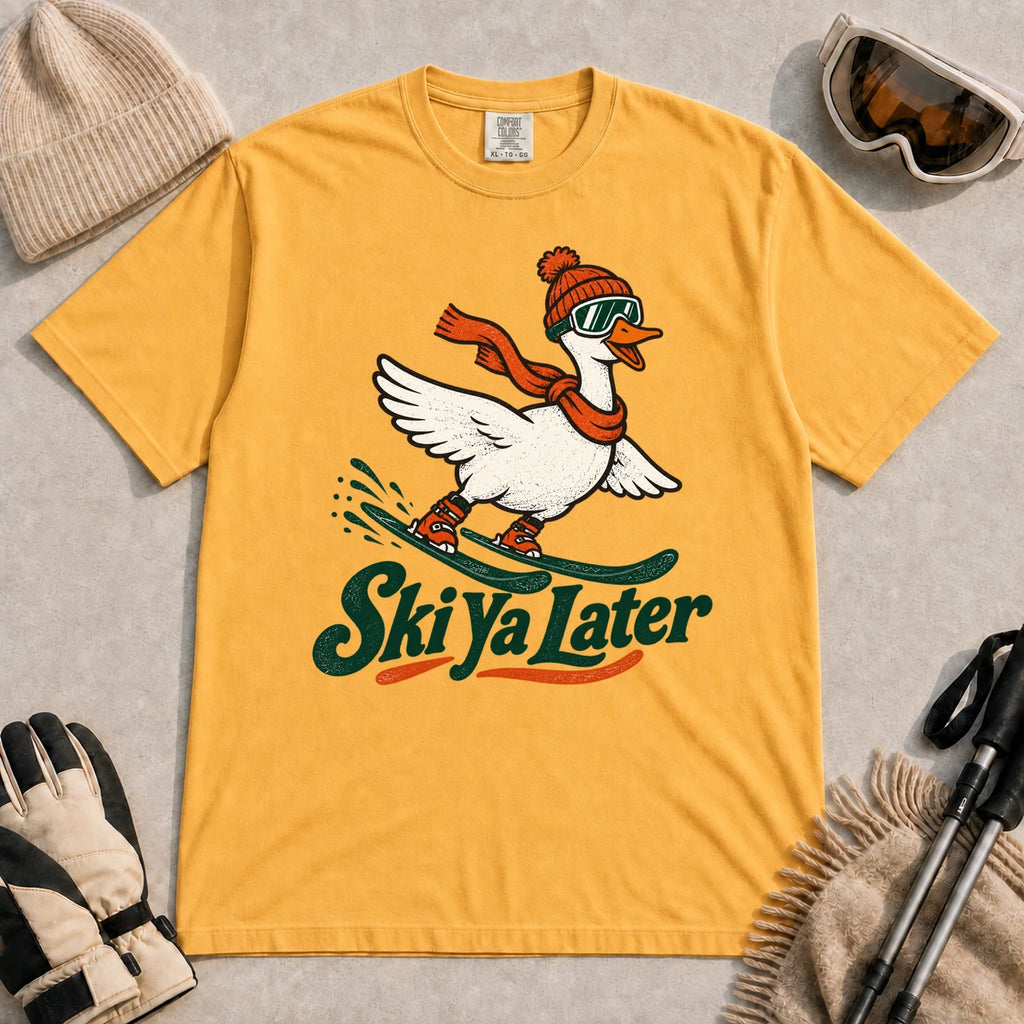 Mustard tee featuring a playful goose skiing in goggles and a beanie above the phrase “On Your Left, Losers.”