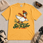 Mustard tee featuring a playful goose skiing in goggles and a beanie above the phrase “On Your Left, Losers.”