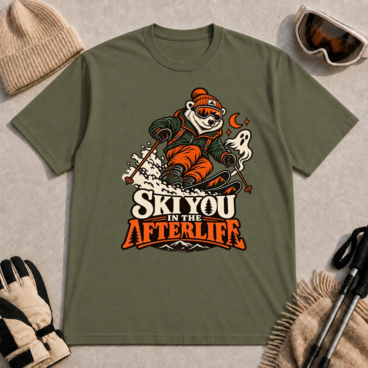 Military Green tee featuring a polar bear skiing through a spooky Halloween scene with a ghost and crescent moon above the phrase “Ski You in the Afterlife.”