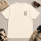 Natural tee featuring minimalist black line art of ski goggles, a ski boot, and an upright ski on the left chest.