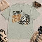 Bay tee featuring a relaxed porcupine in ski goggles lounging in a chair with a hot drink beside a snowboard, with the phrase “Slopes? Maybe Later.”