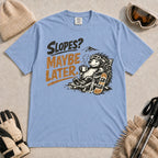 Washed Denim tee featuring a relaxed porcupine in ski goggles lounging in a chair with a hot drink beside a snowboard, with the phrase “Slopes? Maybe Later.”