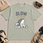 Bay tee featuring a relaxed hedgehog sitting beside ski goggles and a hot drink with the phrase “Slow by Choice.”