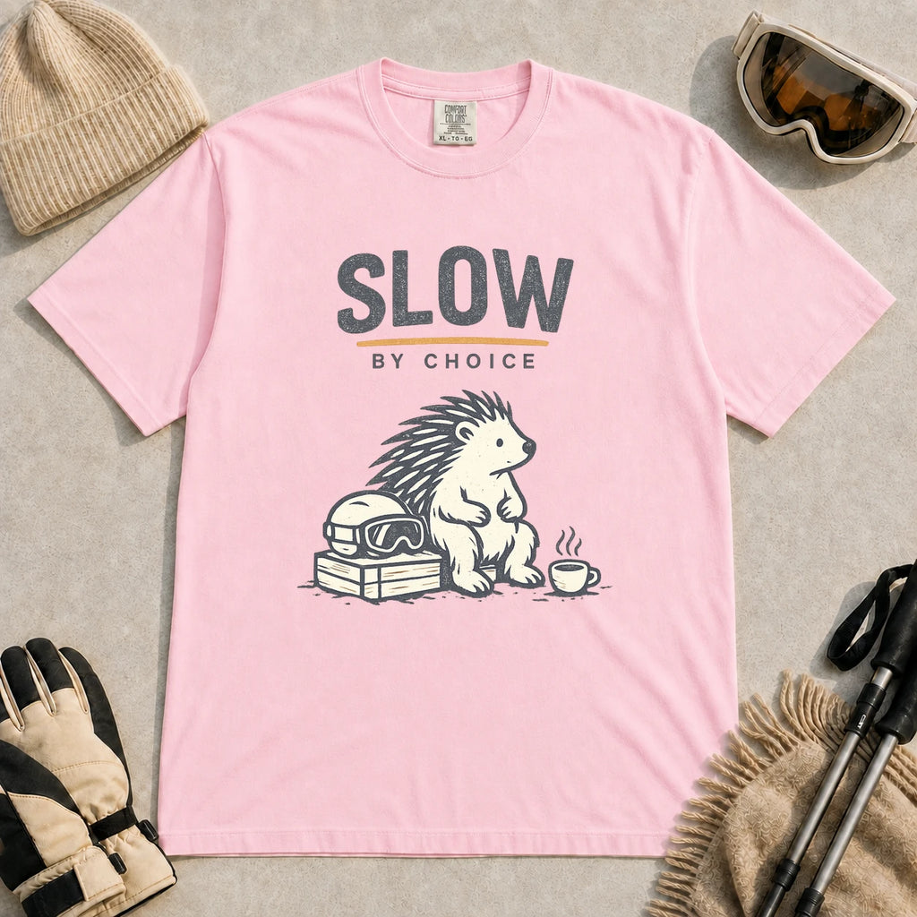 Blossom tee featuring a relaxed hedgehog sitting beside ski goggles and a hot drink with the phrase “Slow by Choice.”