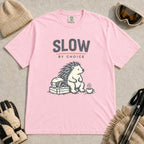Blossom tee featuring a relaxed hedgehog sitting beside ski goggles and a hot drink with the phrase “Slow by Choice.”