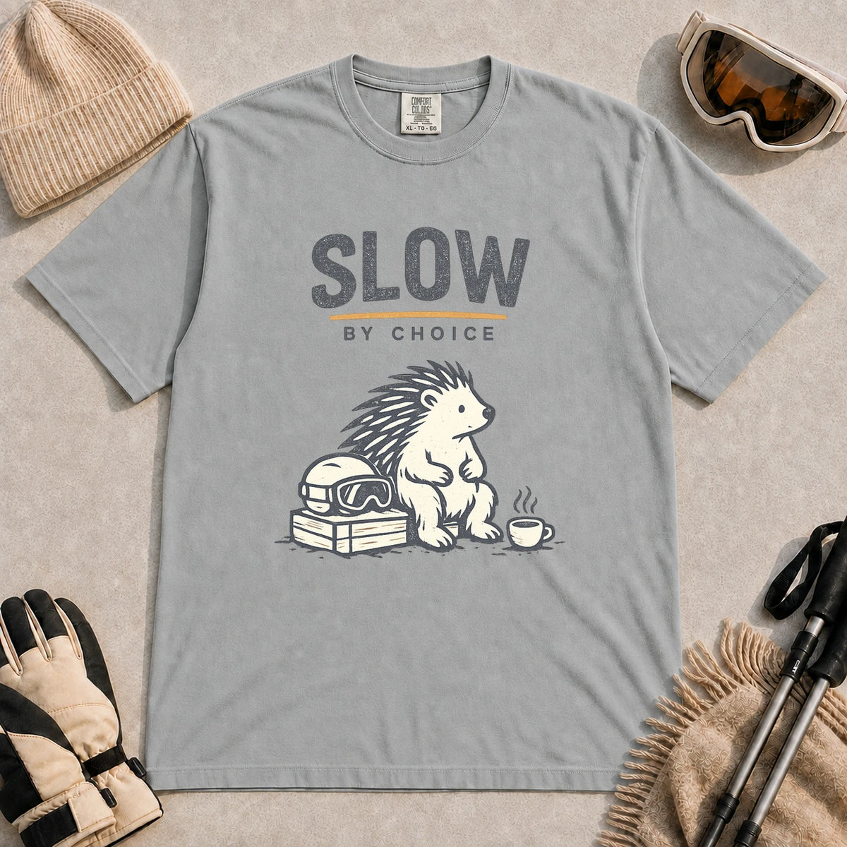 Granite tee featuring a relaxed hedgehog sitting beside ski goggles and a hot drink with the phrase “Slow by Choice.”