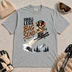 Granite tee featuring a tiny goggle-wearing animal skier launching off a snowy jump, with mountain scenery and the phrase “Small Legs, Big Send.”