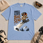 Washed Denim tee featuring a tiny goggle-wearing animal skier launching off a snowy jump, with mountain scenery and the phrase “Small Legs, Big Send.”