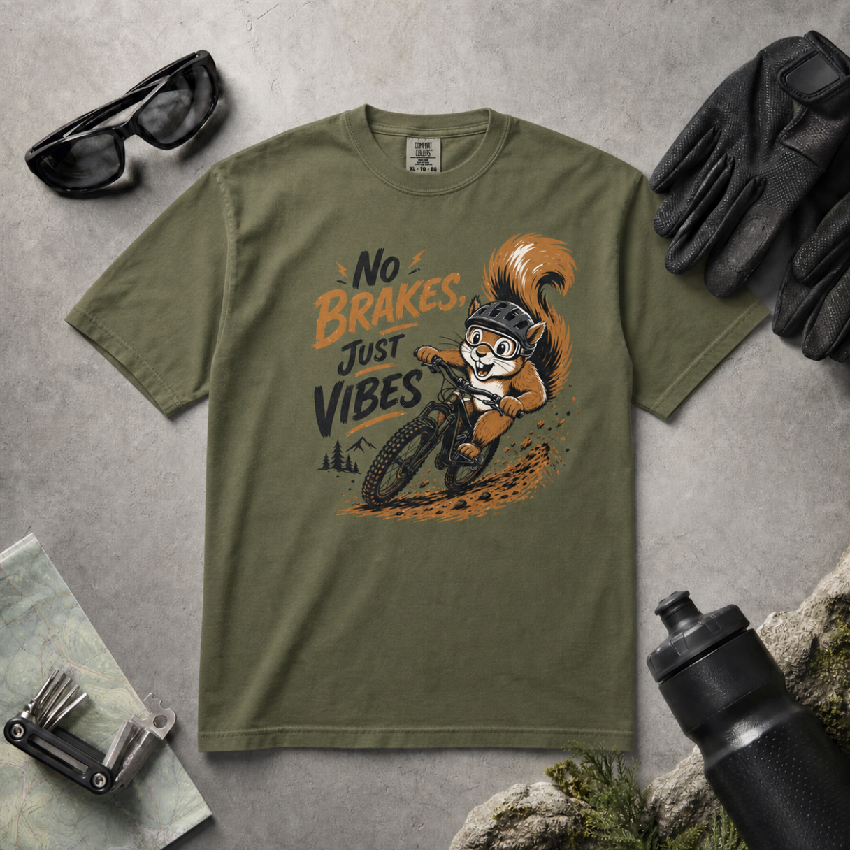 Hemp green t-shirt with a squirrel graphic and text 'No Brakes, Just Vibes' on a gray surface with outdoor accessories.