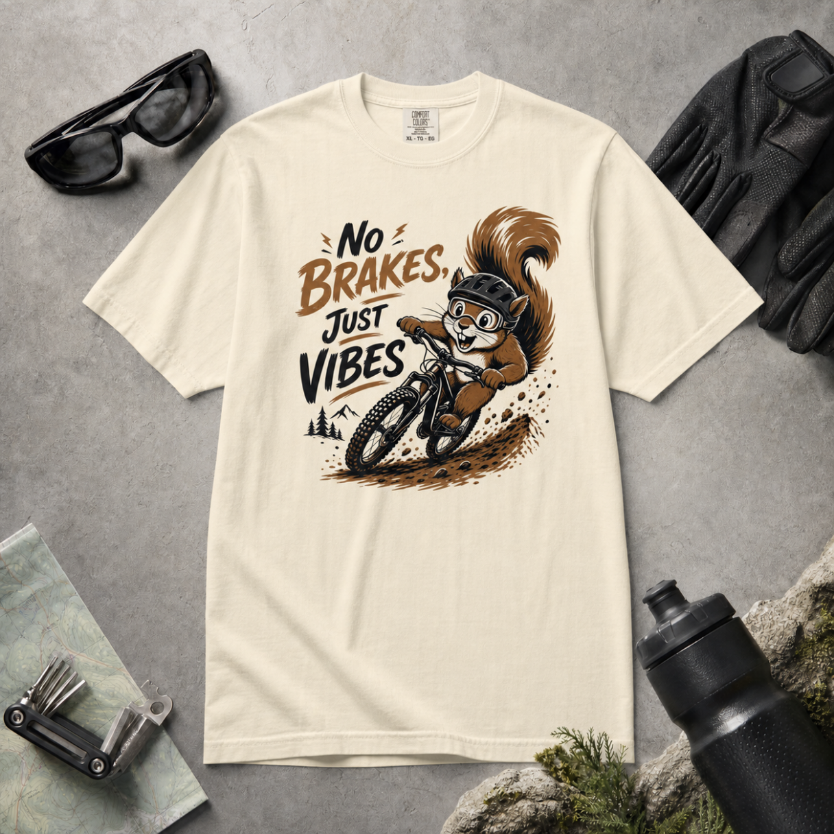 Ivory white t-shirt with a squirrel graphic and 'No Brakes Just Vibes' text on a gray surface with accessories.