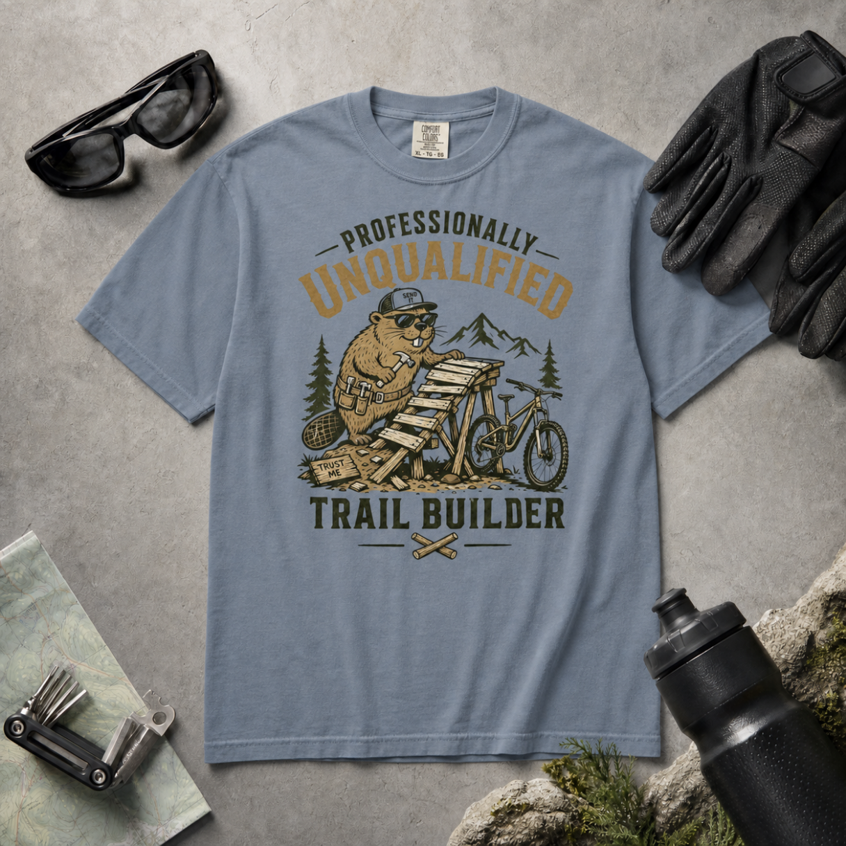 Blue jean colored t-shirt with beaver graphic and text on a gray surface with accessories.