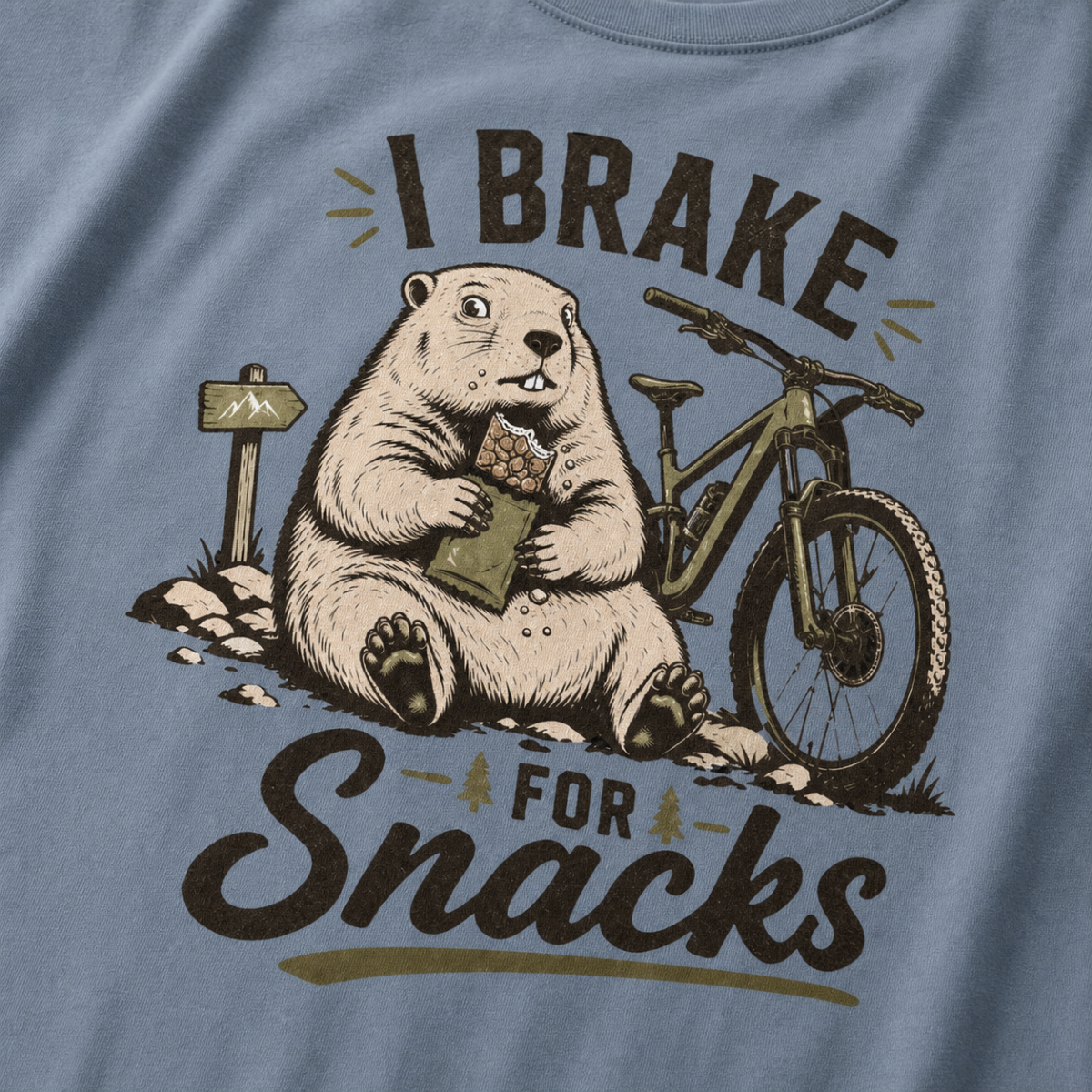 Close-up of a blue jean colored t-shirt with a funny “I Brake for Snacks” graphic showing a snack-loving marmot resting beside a mountain bike.