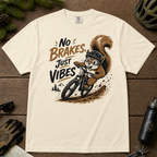 Ivory white t-shirt featuring a squirrel mountain biking down a dirt trail with bold “No Brakes, Just Vibes” lettering.