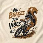Close-up of an ivory white t-shirt featuring a helmeted squirrel riding a mountain bike with “No Brakes, Just Vibes” text.