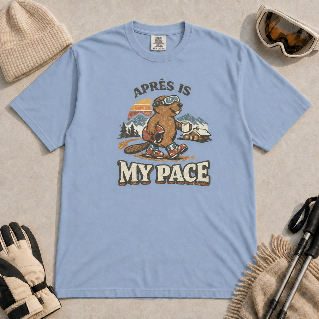 Washed Denim t-shirt featuring an “Après Is My Pace” design with a beaver wearing ski goggles and boots, carrying a helmet and hot drink against a retro mountain and chalet scene.