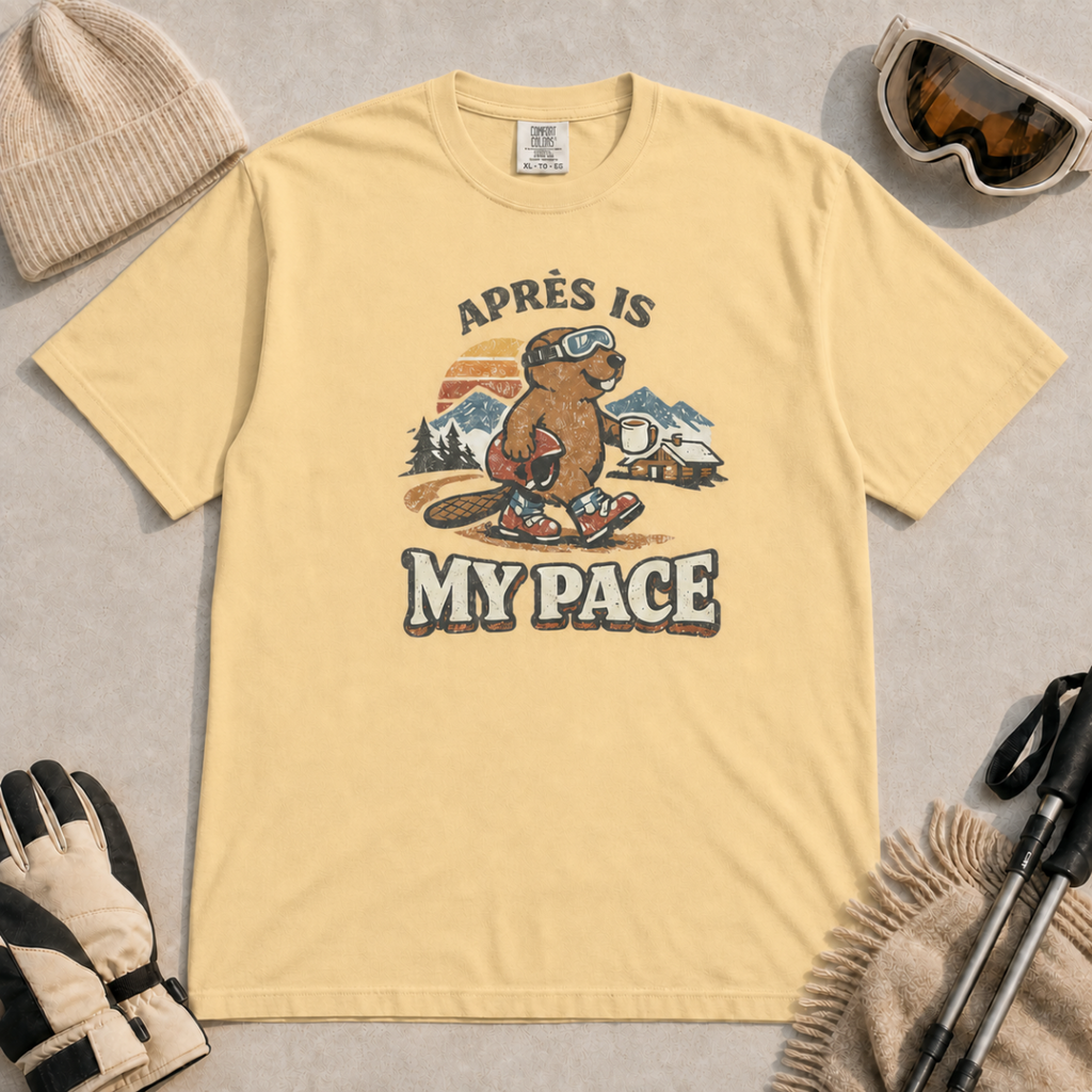 Butter t-shirt featuring an “Après Is My Pace” design with a beaver wearing ski goggles and boots, carrying a helmet and hot drink against a retro mountain and chalet scene.