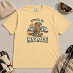 Butter t-shirt featuring an “Après Is My Pace” design with a beaver wearing ski goggles and boots, carrying a helmet and hot drink against a retro mountain and chalet scene.