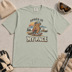 Bay t-shirt featuring an “Après Is My Pace” design with a beaver wearing ski goggles and boots, carrying a helmet and hot drink against a retro mountain and chalet scene.