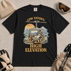 Black t-shirt featuring a vintage raccoon wearing ski goggles and lounging in a gondola with a mug, with the phrase “Low Effort, High Elevation.”