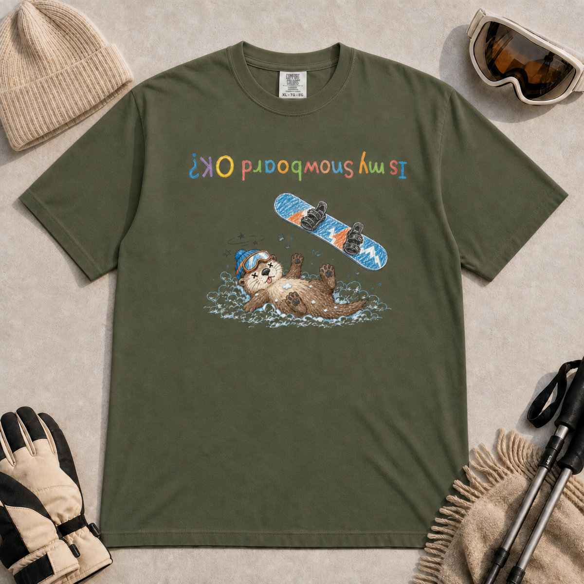 Moss t-shirt featuring a childlike hand-drawn otter lying in the snow beneath a flying snowboard, with the upside-down phrase “Is My Snowboard OK?”