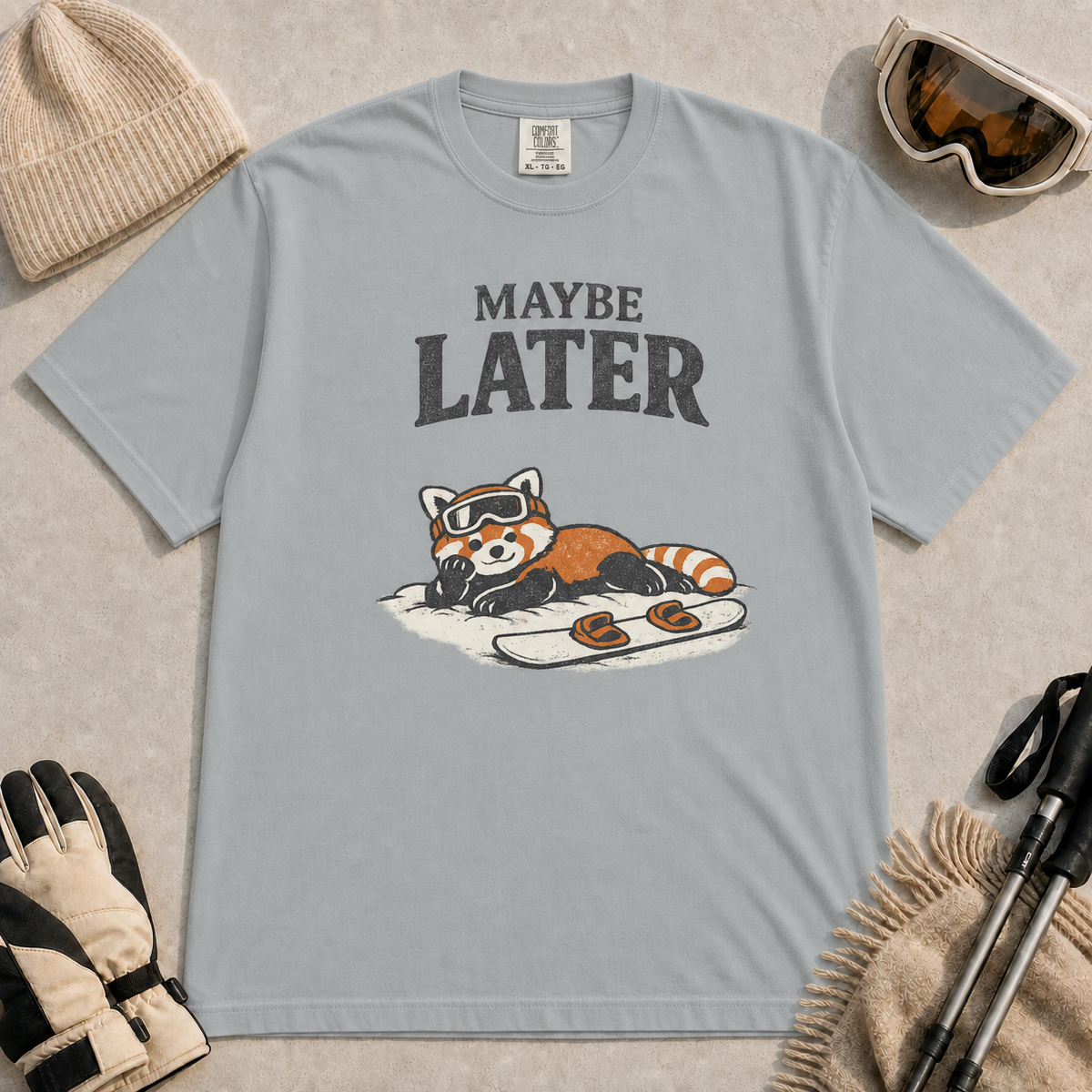 Granite t-shirt featuring a relaxed red panda lying in the snow beside a snowboard, wearing ski goggles beneath the phrase “Maybe Later.”