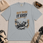 Granite tee featuring a relaxed black bear lounging in a hammock with a steaming mug and checklist beneath the distressed phrase “Busy Taking It Easy.”
