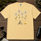 Butter Comfort Colors tee featuring four oversized daisies above a female mountain biker riding alongside a small yellow dog.