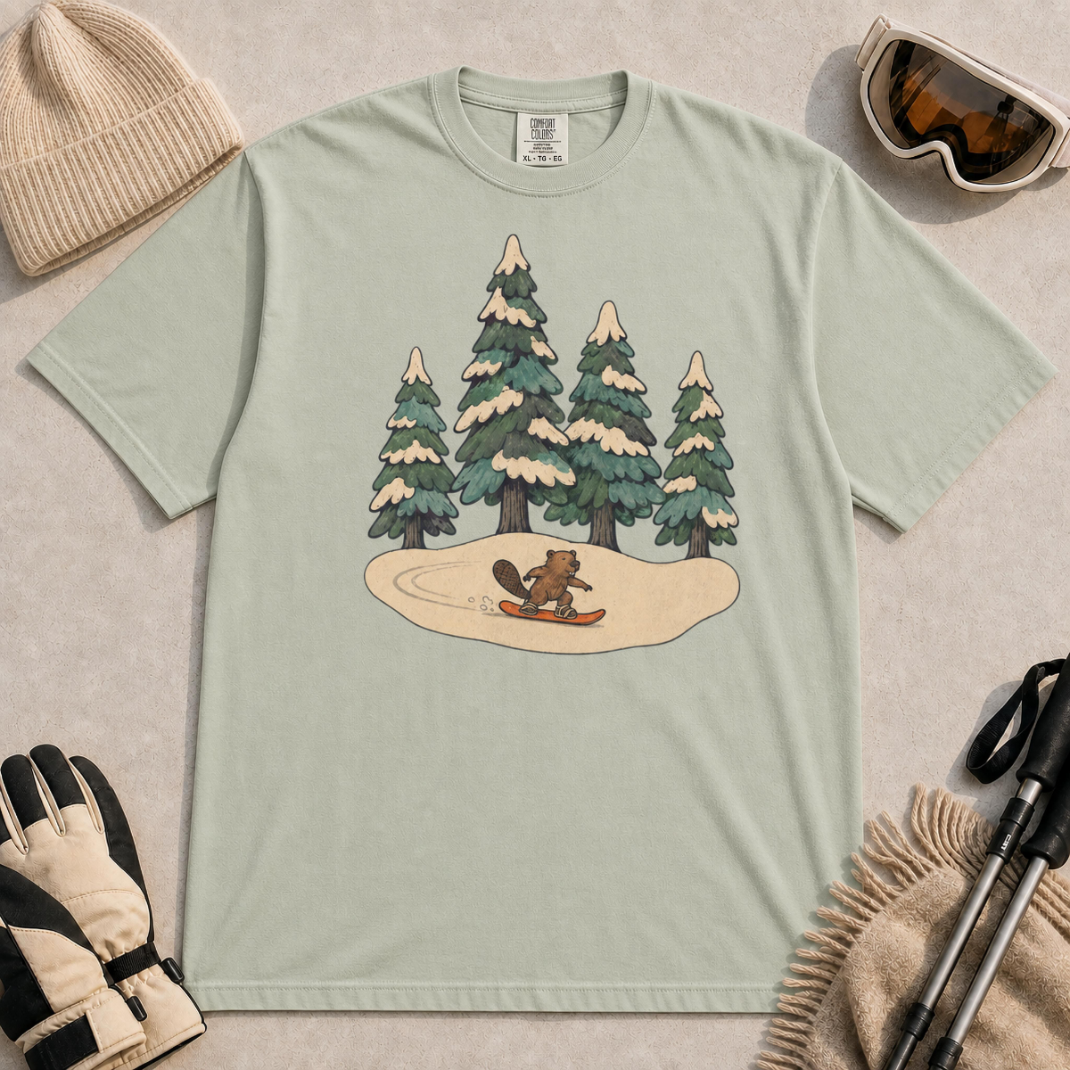 Bay t-shirt featuring a whimsical winter illustration of a small beaver snowboarding across a snowy clearing beneath four snow-covered evergreen trees.