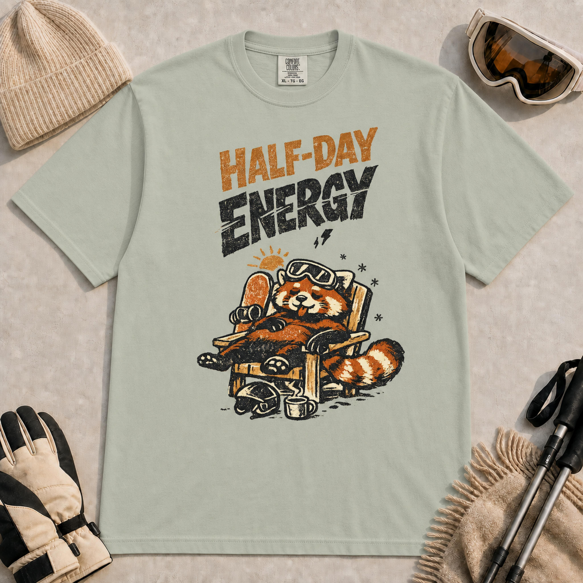 Bay tee featuring a relaxed red panda lounging in a chair with snowboard gear and the phrase “Half-Day Energy.”