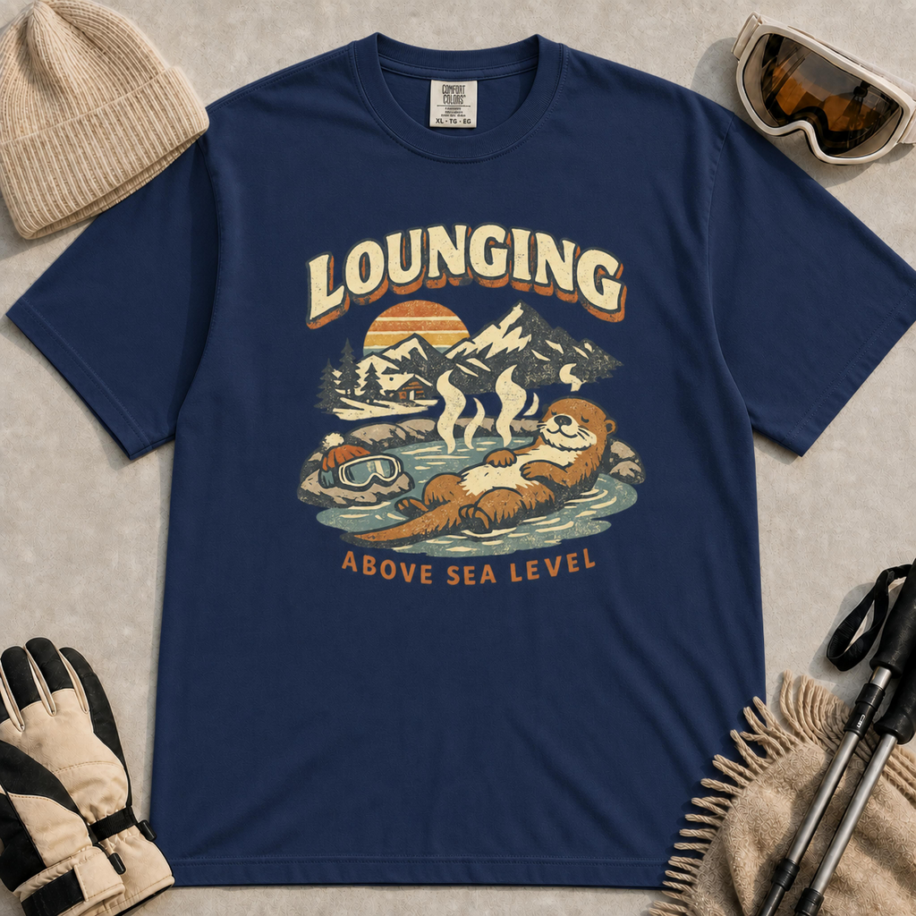 Navy t-shirt featuring a vintage otter lounging in a mountain hot spring beside ski goggles, with the phrase “Lounging Above Sea Level.”