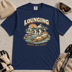 Navy t-shirt featuring a vintage otter lounging in a mountain hot spring beside ski goggles, with the phrase “Lounging Above Sea Level.”
