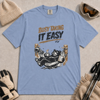 Blue Jean tee featuring a relaxed black bear lounging in a hammock with a steaming mug and checklist beneath the distressed phrase “Busy Taking It Easy.”