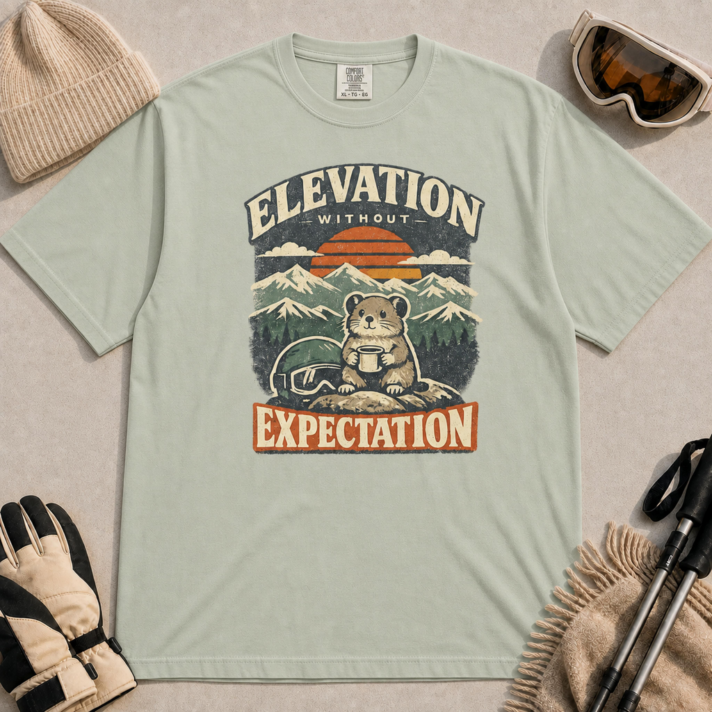 Bay tee featuring a small mountain rodent holding a mug beside ski goggles, with a retro alpine sunset and “Elevation Without Expectation” text.