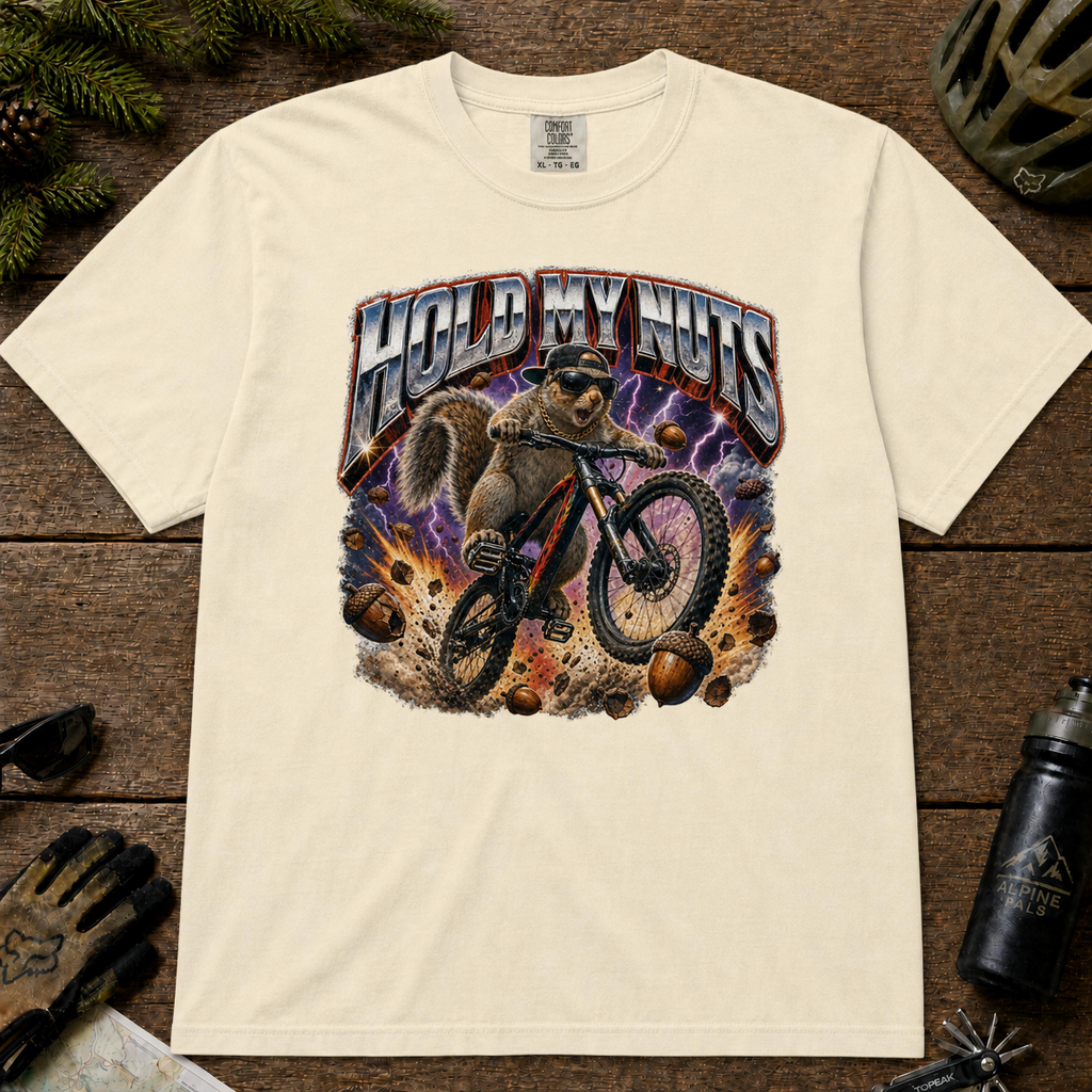 Ivory Comfort Colors tee with a squirrel mountain biking through flying acorns and bold “Hold My Nuts” graphic.