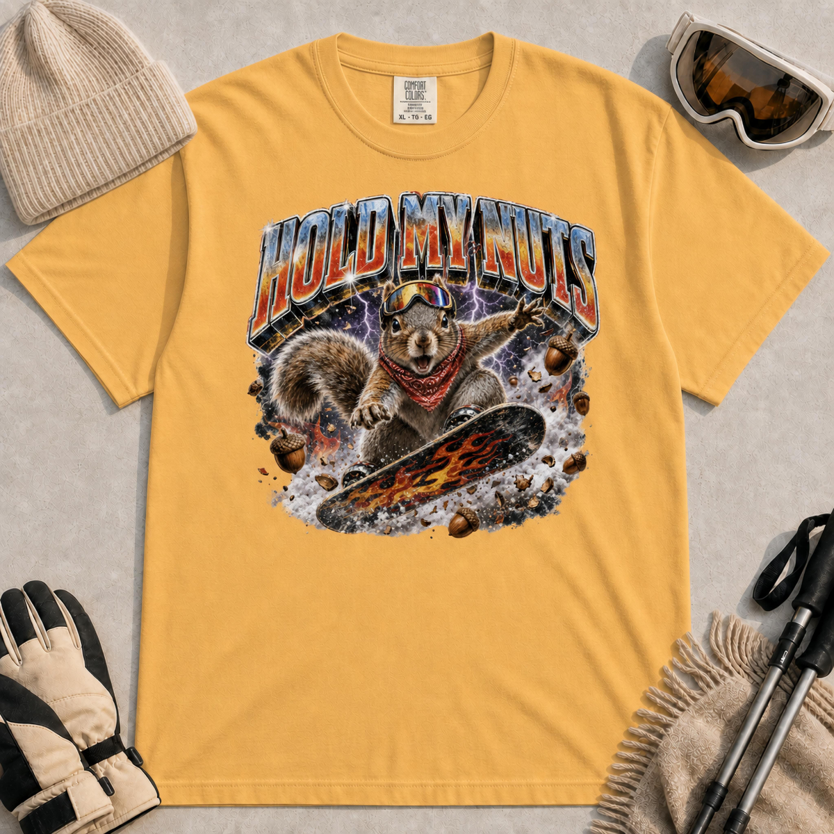 Mustard tee featuring a retro “Hold My Nuts” snowboarding squirrel graphic with flying acorns, lightning, and bold metallic lettering.
