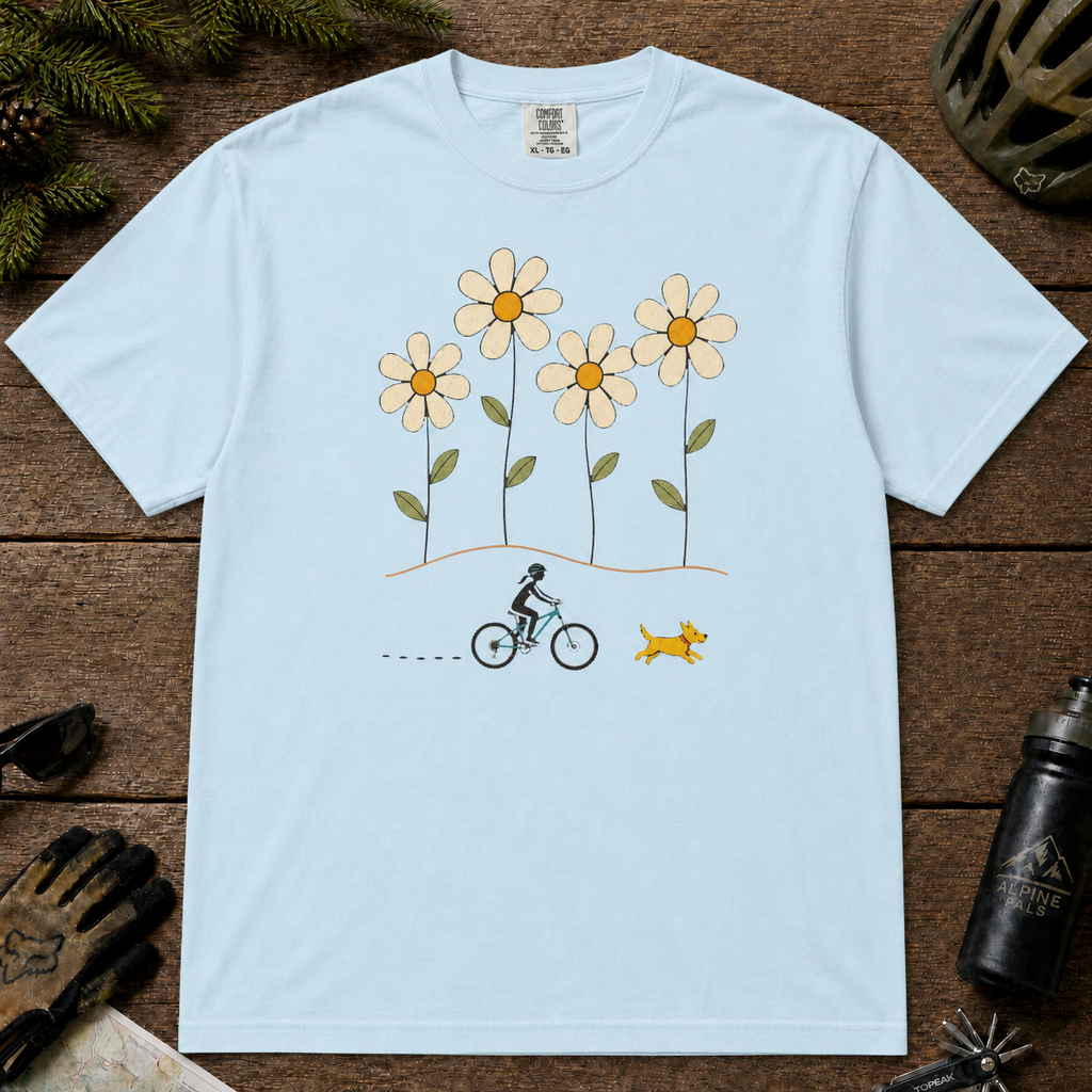 Chambray Comfort Colors tee featuring four oversized daisies above a female mountain biker riding alongside a small yellow dog.
