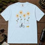 Chambray Comfort Colors tee featuring four oversized daisies above a female mountain biker riding alongside a small yellow dog.