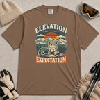 Espresso tee featuring a small mountain rodent holding a mug beside ski goggles, with a retro alpine sunset and “Elevation Without Expectation” text.