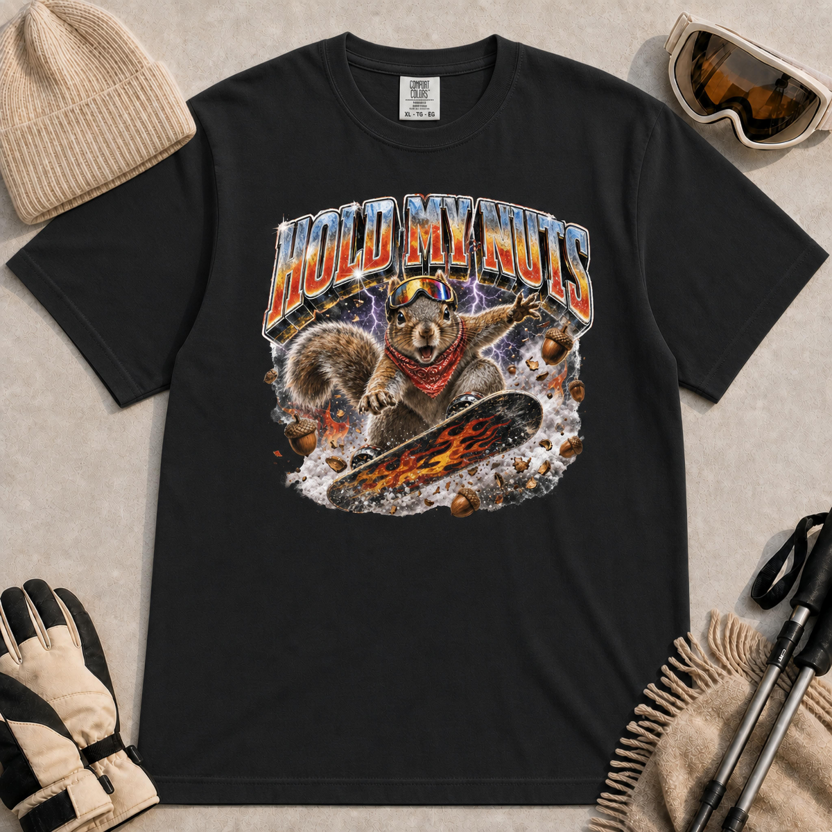 Black tee featuring a retro “Hold My Nuts” snowboarding squirrel graphic with flying acorns, lightning, and bold metallic lettering.