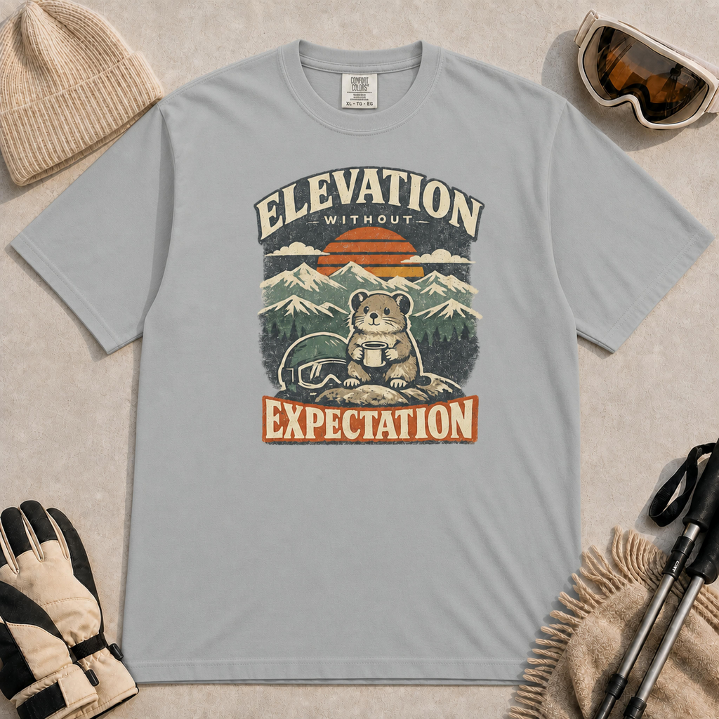 Granite gray tee featuring a small mountain rodent holding a mug beside ski goggles, with a retro alpine sunset and “Elevation Without Expectation” text.