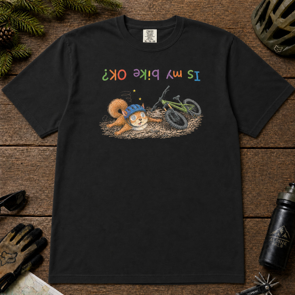 Black t-shirt featuring a childlike hand-drawn squirrel in a bike helmet lying beside a crashed mountain bike, with the upside-down phrase “Is My Bike OK?”