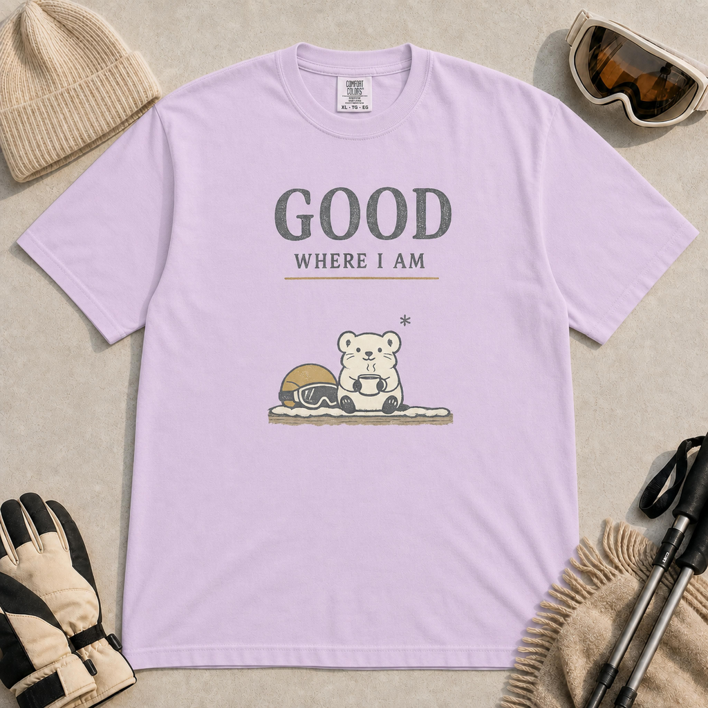 Orchid tee featuring a small polar bear holding a warm mug beside ski goggles, with the phrase “Good Where I Am.”
