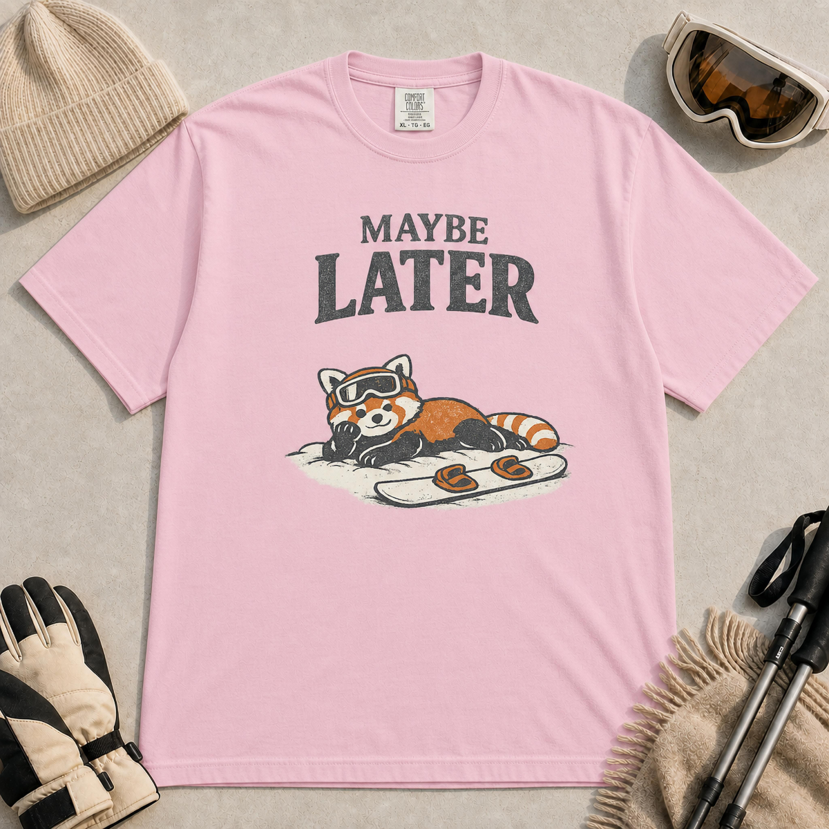 Blossom t-shirt featuring a relaxed red panda lying in the snow beside a snowboard, wearing ski goggles beneath the phrase “Maybe Later.”