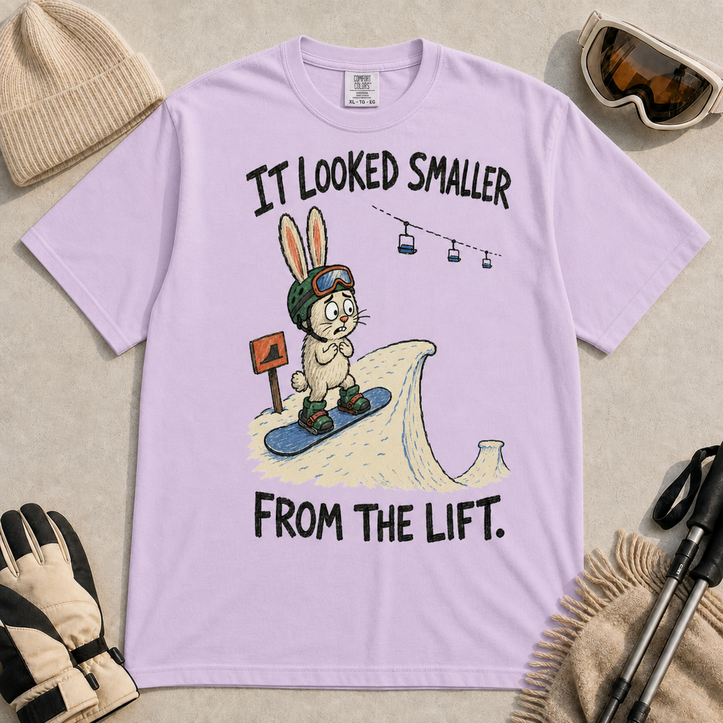 Orchid t-shirt featuring a childlike hand-drawn rabbit snowboarding toward a large snow jump, with the phrase “It Looked Smaller From the Lift.”