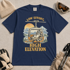 True Navy t-shirt featuring a vintage raccoon wearing ski goggles and lounging in a gondola with a mug, with the phrase “Low Effort, High Elevation.”
