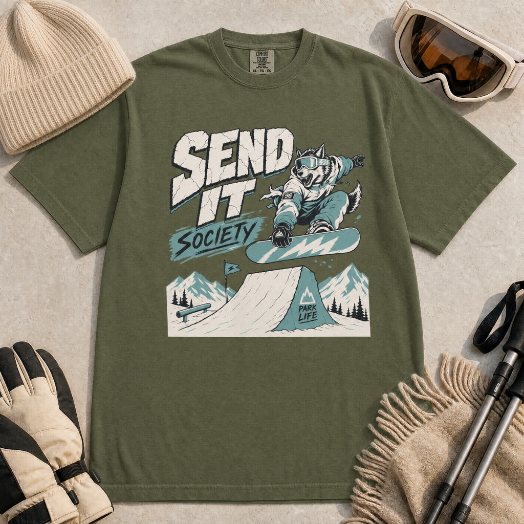 Hemp green t-shirt with a graphic design of a snowboarding wolf and text 'Send It Society' on a beige surface with winter accessories.