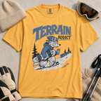 Mustard yellow t-shirt with 'Terrain Addict' graphic on a light gray surface with winter accessories.