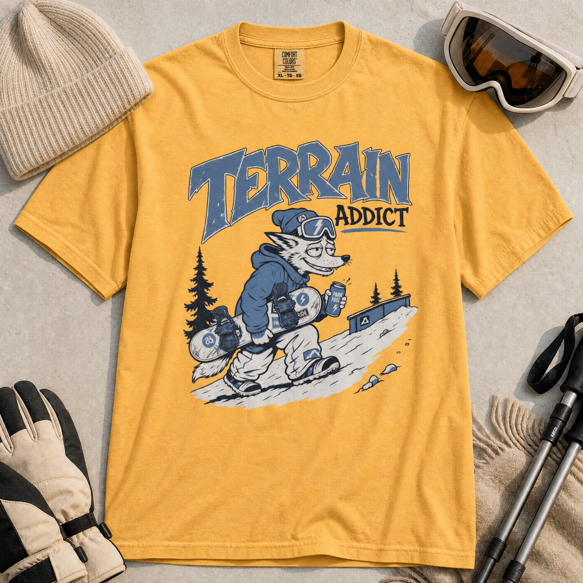 Mustard yellow t-shirt with 'Terrain Addict' graphic on a light gray surface with winter accessories.