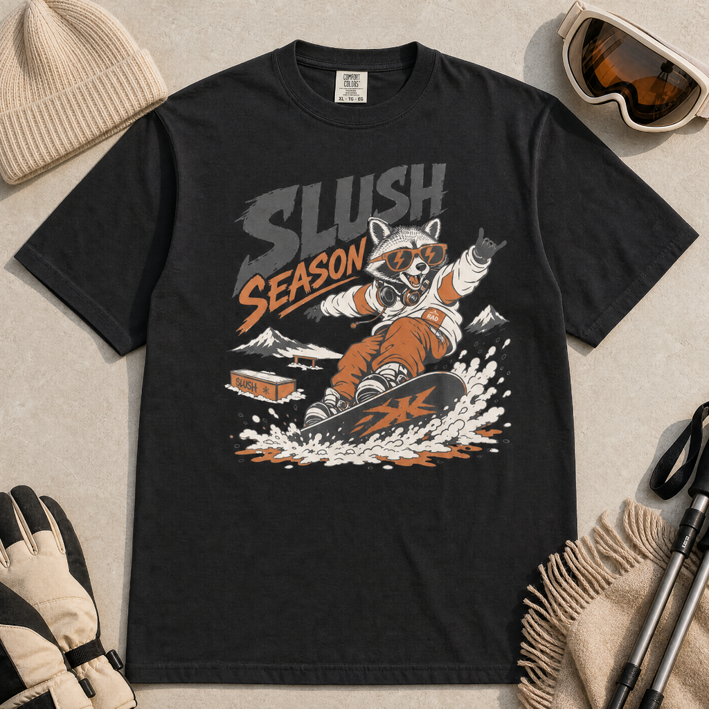 Black t-shirt with 'Slush Season' graphic featuring a raccoon snowboarding, surrounded by winter accessories on a light gray background.