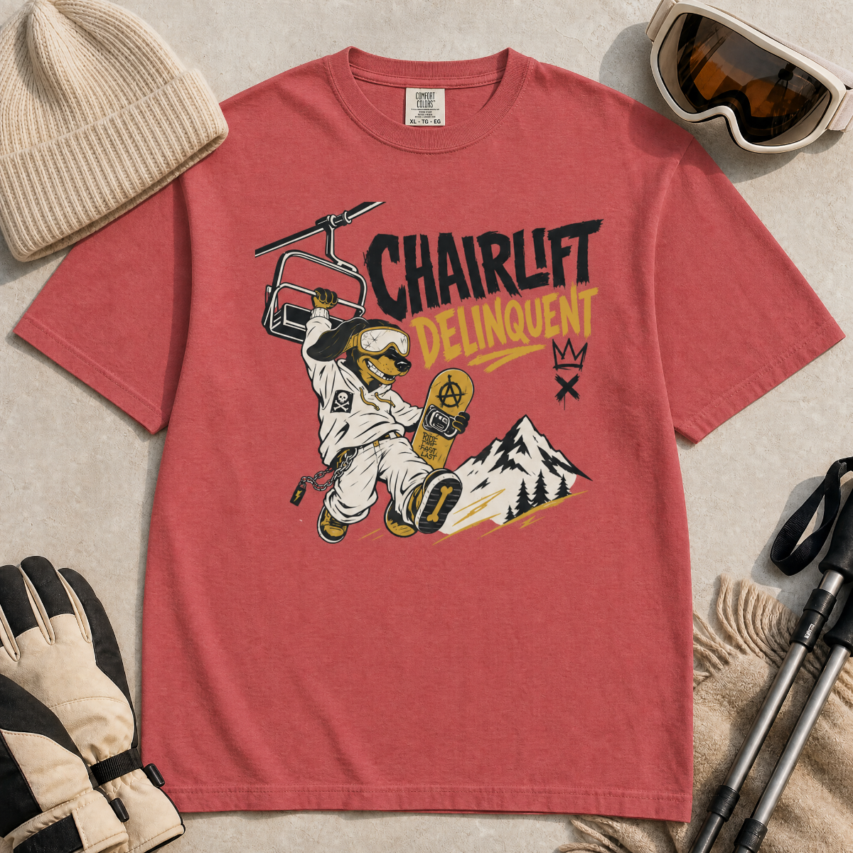 Crimson red t-shirt with a graphic design featuring a dachshund snowboarder and 'Chairlift Delinquent' text, surrounded by winter accessories.